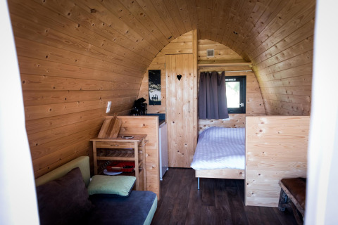 Intérieur du tiny house Treelodge à Gulperberg, Pays-Bas, avec lit, canapé et murs en bois clair.