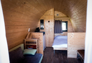 Intérieur du tiny house Treelodge à Gulperberg, Pays-Bas, avec lit, canapé et murs en bois clair.