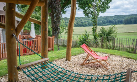 Espace extérieur de la tiny house Treelodge à Gulperberg, Pays-Bas, avec hamac en filet et chaise longue rouge.