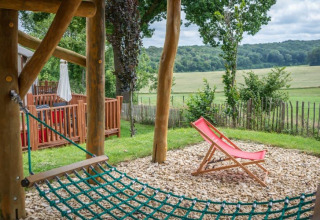 Espace extérieur de la tiny house Treelodge à Gulperberg, Pays-Bas, avec hamac en filet et chaise longue rouge.