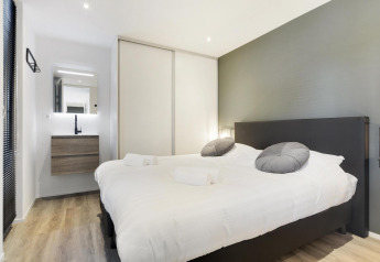 Dormitorio de lodge moderno con cama grande, pared gris, armario empotrado y tocador con espejo.