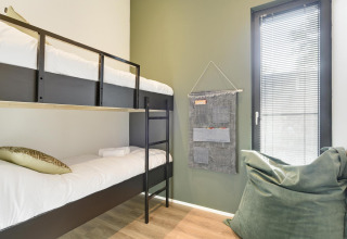 Moderne lodgekamer met stapelbedden, groene zitzak, wandorganizer en raam met jaloezieën.