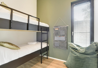 Habitación moderna de lodge con literas, puf verde, organizador colgante y ventana con persianas.