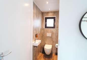 Moderno baño de lodge con paredes de madera, lavabo pequeño, inodoro de pared y ventana arriba.