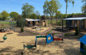 Blick auf Forest Lodge Tiny Houses im Holiday Park 't Rheezerwold, Niederlande, mit Spielplatz im Vordergrund.