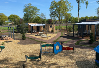 Vista de las tiny houses Forest Lodge en Holiday Park 't Rheezerwold, Países Bajos, con parque infantil delante.