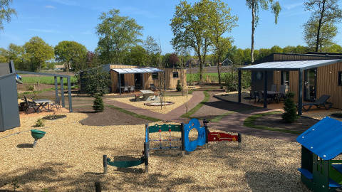Uitzicht op Forest Lodge tiny houses bij Holiday Park 't Rheezerwold in Nederland met speeltuin op de voorgrond.