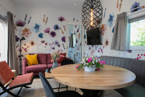 Salon moderne dans un tiny house avec papier peint floral coloré, table ronde en bois et canapé cosy.
