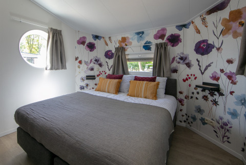 Dormitorio de una tiny house Forest lodge en Holiday Park 't Rheezerwold, Países Bajos, con pared floral.