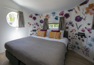 Schlafzimmer im Forest Lodge Tiny House im Holiday Park 't Rheezerwold, Niederlande, mit Blumenwand.