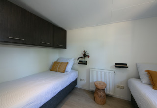 Schlafzimmer der Forest Lodge im Ferienpark 't Rheezerwold, Niederlande, mit zwei Einzelbetten.