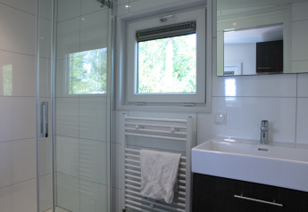 Salle de bains moderne avec douche, fenêtre, sèche-serviettes et lavabo au Forest lodge aux Pays-Bas.