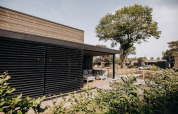 Modern exterior of a Luxury Lodge at Soof Retreats in the Netherlands, featuring a deck and garden seating.