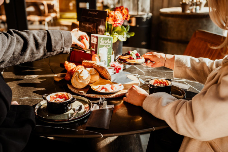 Zwei Personen genießen ein luxuriöses Frühstück mit Brot, Obst und Kaffee im Luxury Family Water Lodge.