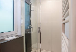 Baño moderno con ducha de vidrio, inodoro suspendido y suelo de madera en Urban-Gardens Lodge en Bélgica.