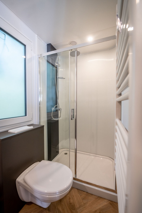 Baño moderno con ducha de vidrio, inodoro suspendido y suelo de madera en Urban-Gardens Lodge en Bélgica.