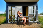 Una mujer y un niño se sientan en la terraza de una cabaña Comfort Lodge en Kompas Camping Westende en Bélgica.