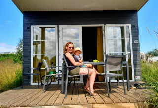 Una mujer y un niño se sientan en la terraza de una cabaña Comfort Lodge en Kompas Camping Westende en Bélgica.