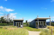 Dos casas pequeñas en Comfort Lodge, Kompas Camping - Westende, Bélgica, con cielo azul y césped verde.
