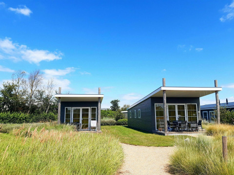 Two small lodges at Comfort Lodge, Kompas Camping - Westende in Belgium, surrounded by grass and blue sky.