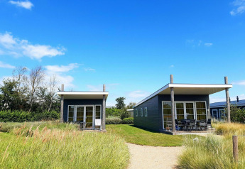 Deux lodges à Comfort Lodge, Kompas Camping - Westende en Belgique, sous un ciel bleu et entourés d’herbe verte.