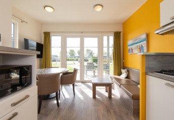 Bright glamping accommodation interior with dining table, sofa, kitchenette, and garden view.