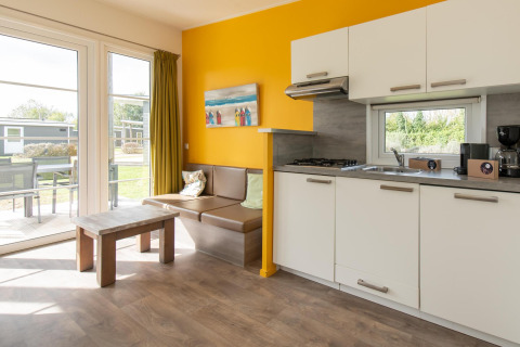 Moderne glamping accommodatie met keuken, zithoek, grote ramen en toegang tot terras in het groen.