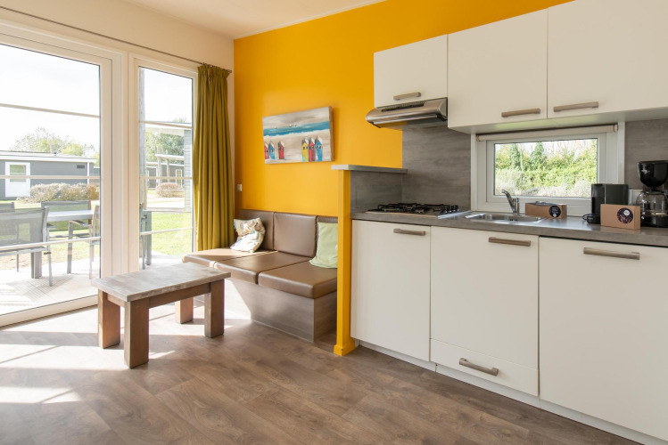 Alojamiento glamping moderno con cocina, zona de estar, grandes ventanas y acceso a patio natural.