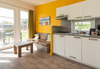 Sistemazione glamping moderna con cucina, angolo salotto, ampie finestre e accesso al patio nella natura.