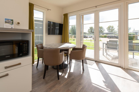 Bright dining area in Comfort Lodge at Kompas Camping Westende, Belgium, with modern furniture and garden view.