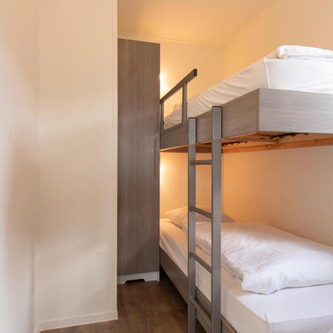 Kleine glampingkamer met stapelbed, moderne kleerkast en een lichte, gezellige inrichting.