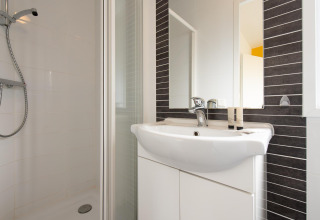 Moderne badkamer met douche, lavabo en spiegel in een gezellige glamping accommodatie.