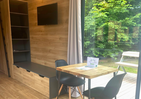 Interior de Tiny Home en Urban-Gardens, Bélgica, con mesa de comedor, sillas, estantes y vista al jardín.