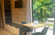 Interior de Tiny Home en Urban-Gardens, Bélgica, con mesa de comedor, sillas, estantes y vista al jardín.