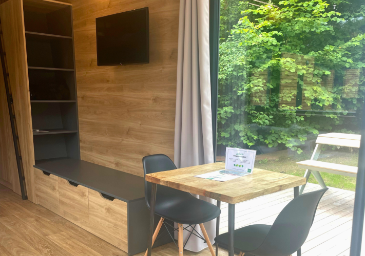 Interieur van de Tiny Home bij Urban-Gardens in België met eettafel, stoelen, planken en tuinzicht.