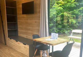 Interior de Tiny Home en Urban-Gardens, Bélgica, con mesa de comedor, sillas, estantes y vista al jardín.