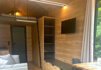 Interior moderno de una tiny house en Urban-Gardens, Bélgica, con altillo, TV y paredes de madera.