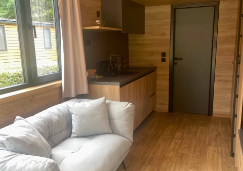 Interiør af Tiny Home ved Urban-Gardens i Belgien med sofa, tekøkken og vindue med udsigt.