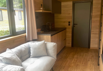 Intérieur du Tiny Home aux Urban-Gardens en Belgique, avec canapé, kitchenette et grande fenêtre.