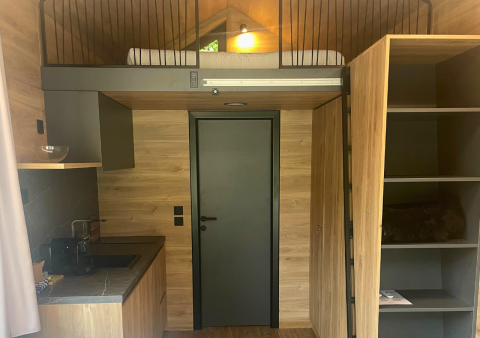 Vista interior de Tiny Home en Urban-Gardens, Bélgica, con cama alta, cocina y paredes de madera.