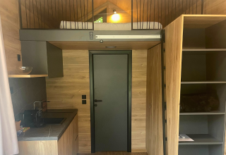 Vista interior de Tiny Home en Urban-Gardens, Bélgica, con cama alta, cocina y paredes de madera.