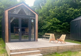 Klein houten huisje met terras, twee stoelen en tafel, omringd door bomen in Urban-Gardens, België.