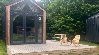 Piccola casa in legno con terrazza, due sedie e tavolo, immersa negli alberi a Urban-Gardens, Belgio.