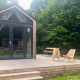 Kleines Holzhaus mit Terrasse, zwei Stühlen und Tisch, umgeben von Bäumen in Urban-Gardens Belgien.