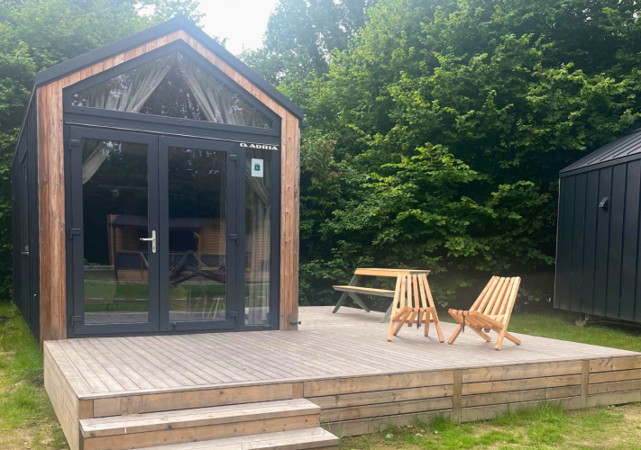 Klein houten huisje met terras, twee stoelen en tafel, omringd door bomen in Urban-Gardens, België.