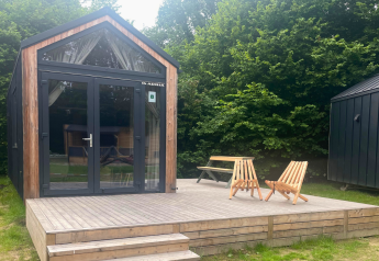 Kleines Holzhaus mit Terrasse, zwei Stühlen und Tisch, umgeben von Bäumen in Urban-Gardens Belgien.