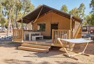 Alojamiento glamping Villatent Outback con porche delantero, bancos y hamaca entre árboles.