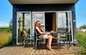 Mujer con niño sentada fuera de Comfort Lodge en Kompas Camping Westende, Bélgica, en un día soleado.