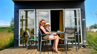 Vrouw met kind zittend op terras van Comfort Lodge bij Kompas Camping Westende, België, zonnige dag.