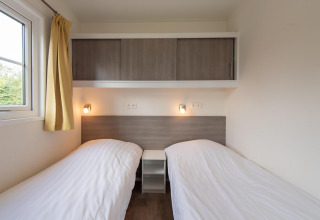 Twee eenpersoonsbedden met witte lakens in Comfort Lodge bij Kompas Camping Westende, honden welkom.